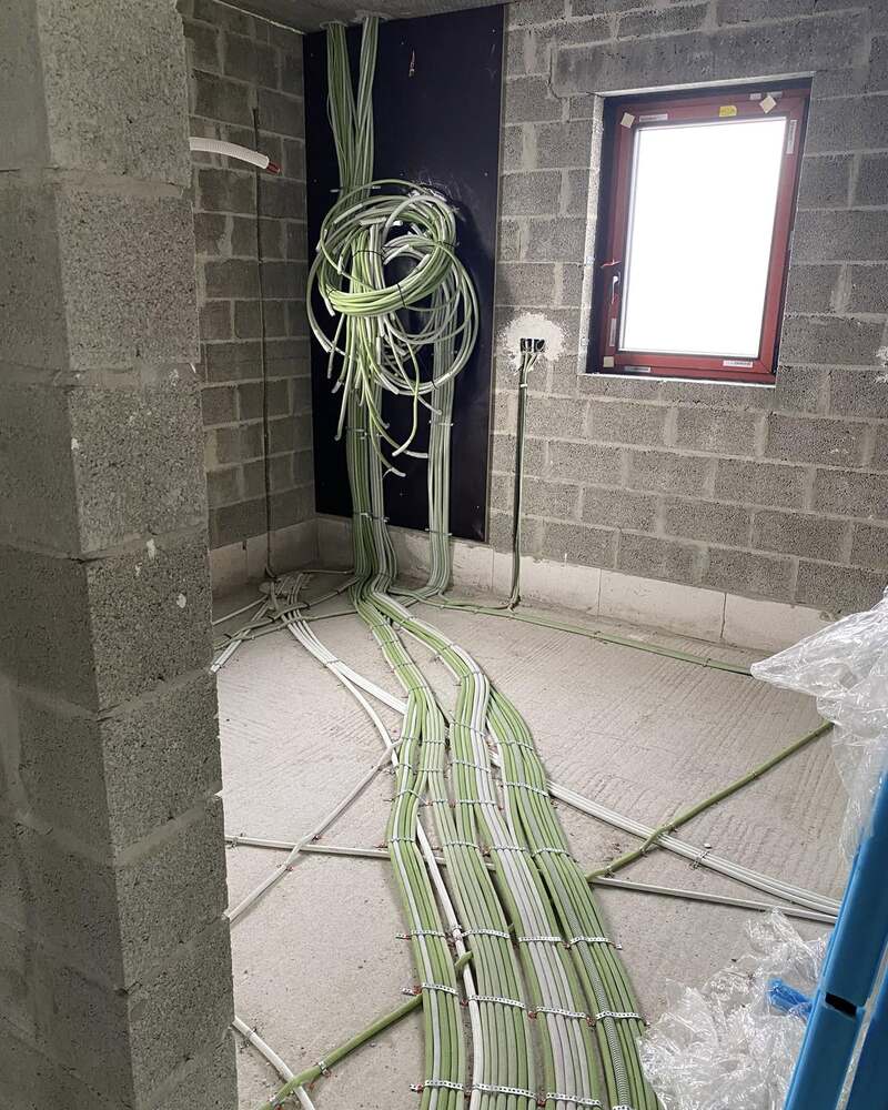 Chantier au stade du gros œuvre : faisceau de câbles électriques en attente dans un angle, gaines au sol.