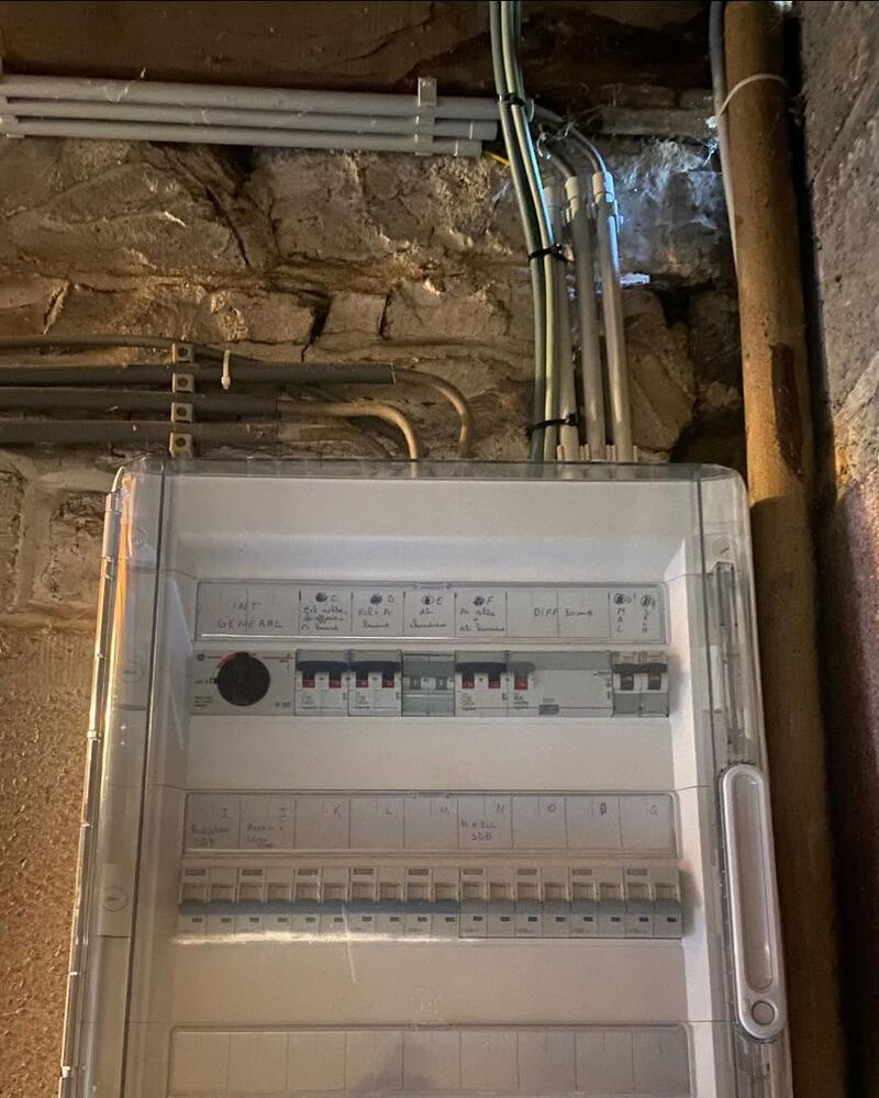 Coffret électrique dans une cave : disjoncteurs sous capot transparent, circuits étiquetés, gaines au plafond.