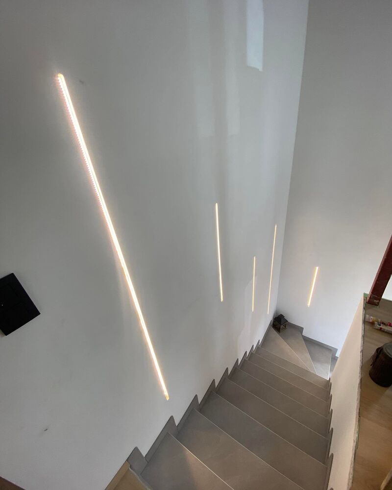 Escalier le long d’un mur blanc où courent des lignes LED encastrées.