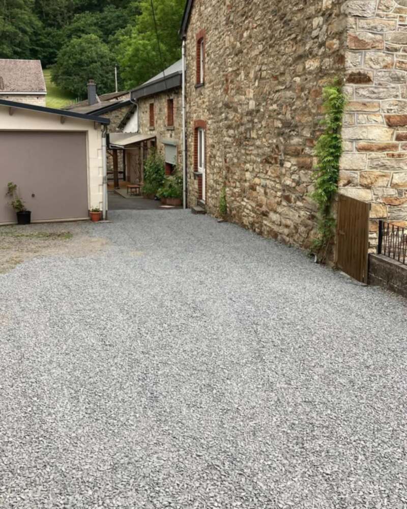 Cour en gravier remise au propre devant des garages et une maison en pierre.