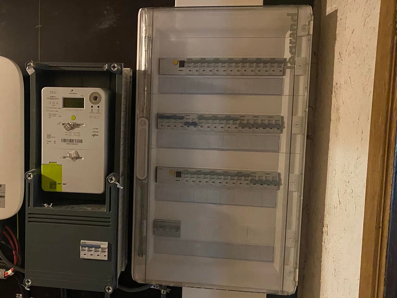 Compteur électrique et tableau modulaire sous capot transparent, fixés sur un panneau.